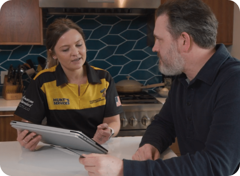 Technician from Hunt's Services discussing home maintenance solutions with a homeowner, using a tablet in a kitchen setting.