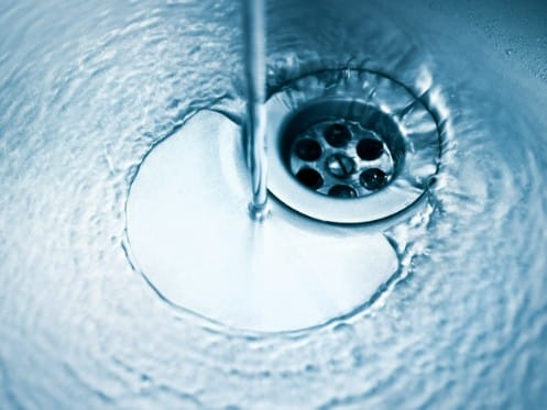 Water flowing down a kitchen sink drain, highlighting plumbing functionality and maintenance importance for home systems.