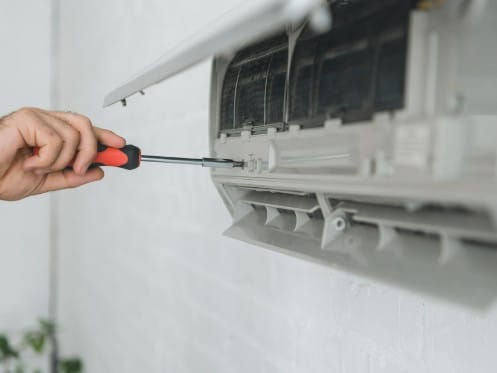 Male worker using a screwdriver to repair a ductless mini-split air conditioning system.