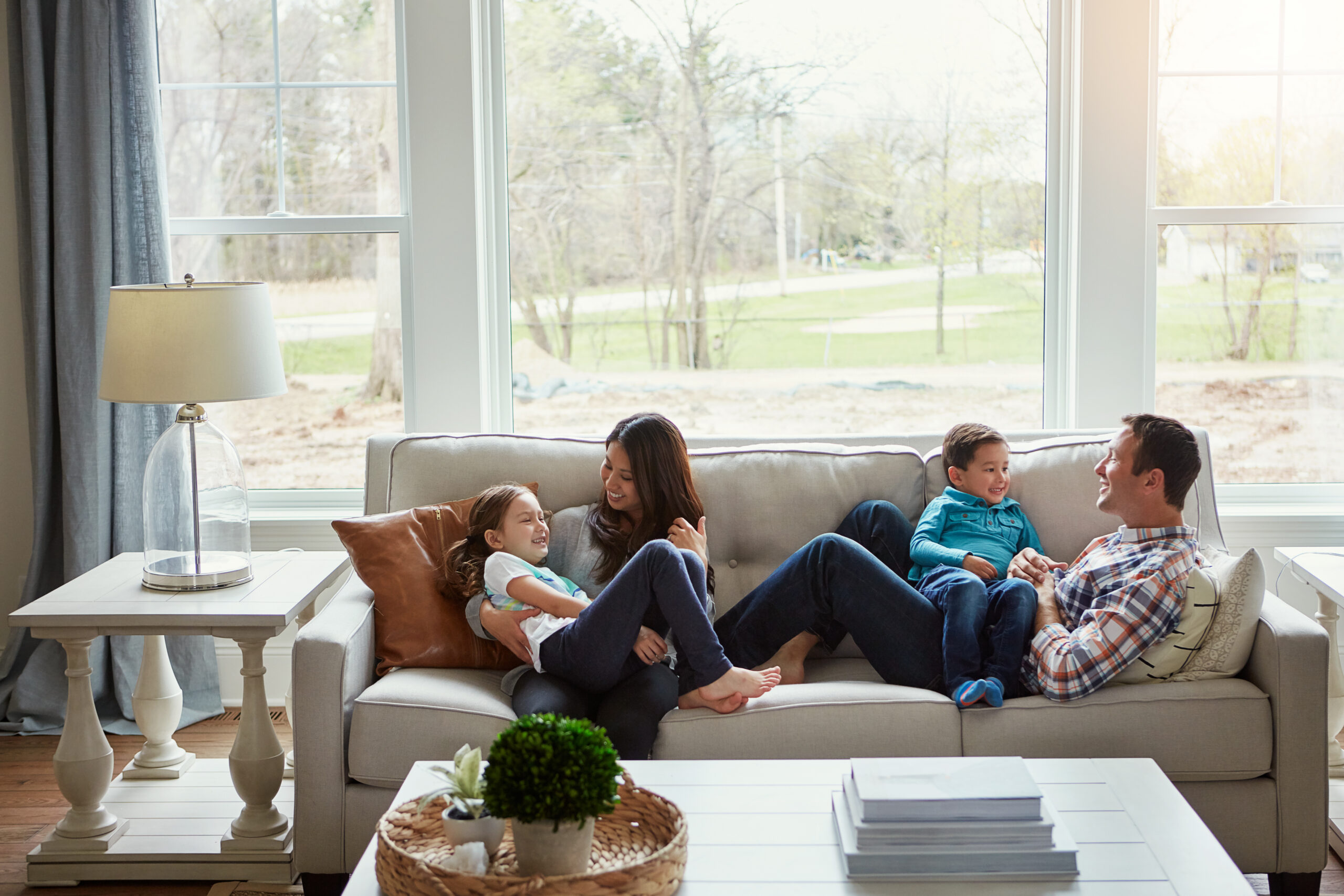 Family enjoying quality time together on a cozy couch in a bright living room, with a lamp and decorative table in the foreground.