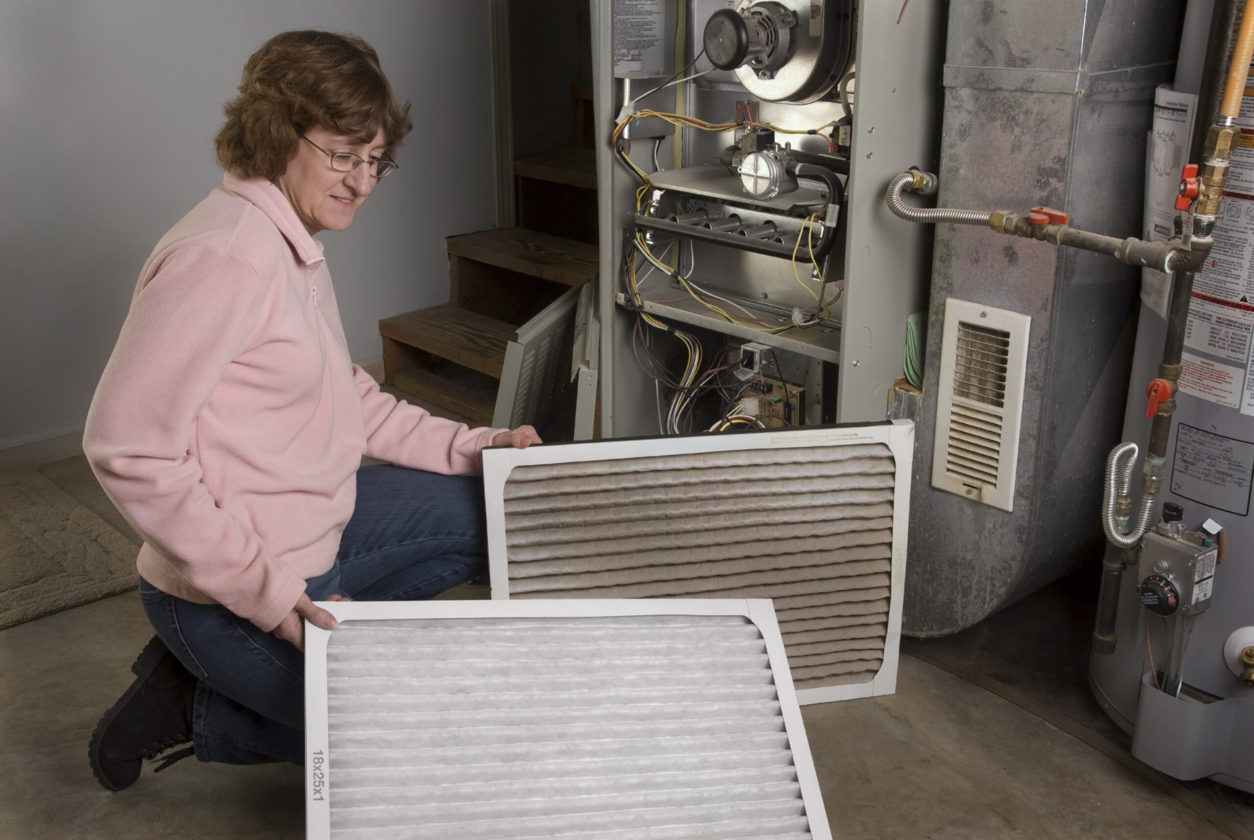 Woman replacing furnace filters while inspecting an HVAC system, emphasizing the importance of regular maintenance for indoor air quality.