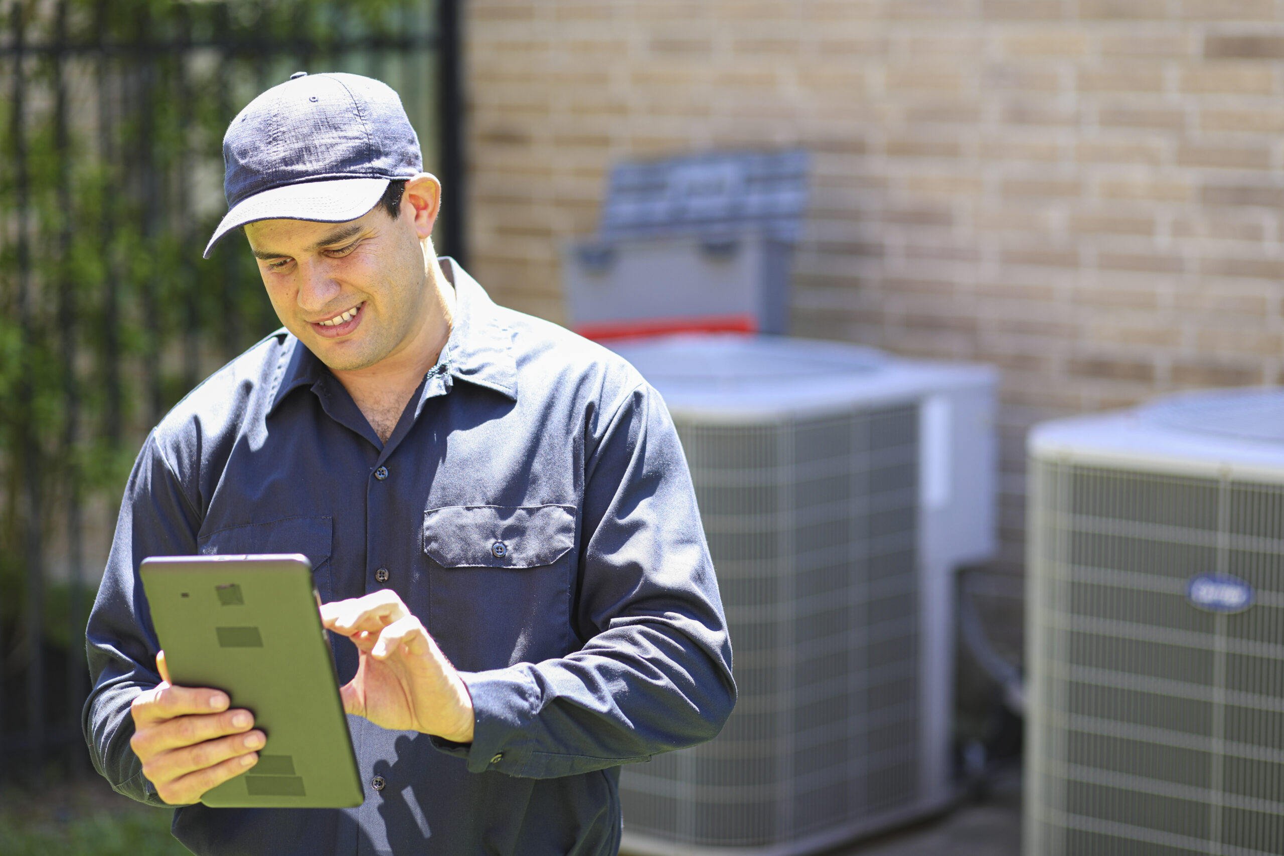 HVAC technician using a tablet outdoors near air conditioning units, emphasizing home maintenance and service efficiency.