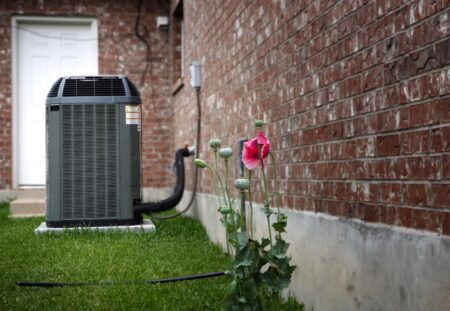 HVAC unit installed outside a brick home with green grass and blooming flowers, emphasizing the importance of HVAC maintenance for homeowners.