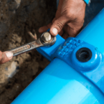 Person using a wrench to tighten a blue plumbing pipe fitting, illustrating professional plumbing services and emergency repairs by Hunt's Services.