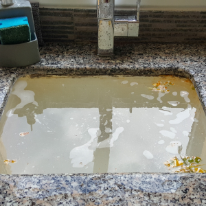 Clogged kitchen sink filled with dirty water and debris, illustrating common plumbing issues related to drain blockages.