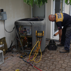 HVAC technician from Hunt's Services inspecting and servicing an outdoor air conditioning unit during a pre-winter maintenance check.