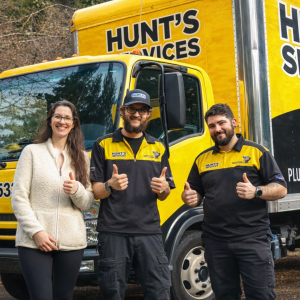 Hunt's Services team members and a woman giving thumbs up in front of a bright yellow service truck, representing community support and home repair assistance for families in need.